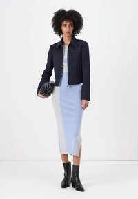Marineblå kuttjakke over en lys blå og grå ribbet midikjole; tilbehør med en svart clutch og ankelstøvler. Glatt stofftekstur.