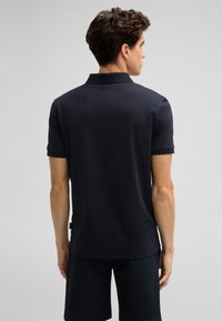 Granatowa koszulka polo wykonana z gładkiego materiału, z klasycznym kołnierzykiem i krótkimi rękawami. Noszona z ciemnymi, fakturowanymi szortami.