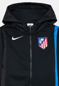 Melnā Nike jaka ar kapuci, ar zilajiem sānu akcentiem un izšūtu komandas emblēmu. Priekšpuse ar rāvējslēdzēju un gludu tekstūru.