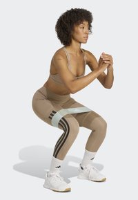 Leggings atléticos beige con rayas negras, combinados con un sujetador deportivo a juego y zapatillas blancas. Una banda de resistencia azul clara está colocada por encima de las rodillas.