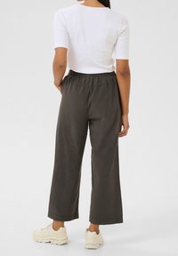 Pantalon large vert olive foncé à taille élastique, porté avec un haut blanc ajusté et des chaussures de sport claires.