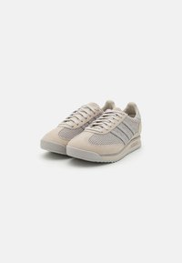 Jasne beżowe sneakersy z teksturowanym, dzianinowym wierzchem, zamszowymi akcentami, symetrycznym wzorem sznurowania oraz gumową podeszwą z bieżnikiem.
