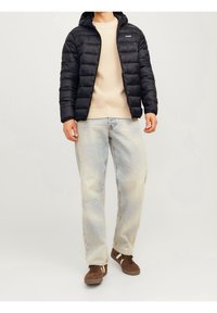 Sort dunjakke med hætte, beige striktrøje og lyseblå jeans. Brune sneakers med hvide striber fuldender outfittet.