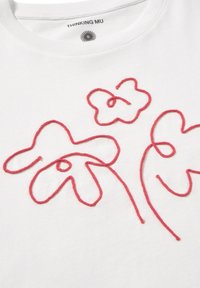 Vit bomulls-T-shirt med röda broderade blommönster med böjda linjer och slingor. Märkets etikett är tryckt på insidan av halsringen.