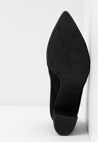 Semelle de chaussure noire à bout pointu avec dessins de pièces en relief, texte "KAISER" et talon indiquant la taille 4½ ainsi que la marque "Peter Kaiser Germany".