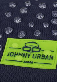 Námorná tkanina s vyvýšenými priesvitnými kvapkami. Obsahuje jasne zelenú nášivku s logom "JOHNNY URBAN JUNIOR" v embosovanom modrom texte.
