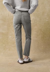 Graue Jeanshose mit geradem Schnitt, ausgefranstem Saum und zwei Gesäßtaschen, kombiniert mit weißen Sneakern mit schwarzen Streifen.