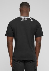 Sort bomulds T-shirt med rund halsudskæring. Denne T-shirt har et hvidt grafisk motiv på ryggen. Korte ærmer og afslappet pasform. Ingen synlige mønstre eller detaljer.