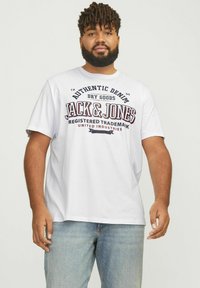 Hvit bomulls T-skjorte med et stort grafisk trykk av "JACK & JONES" i burgunder og svart. Korte ermer og rund hals.