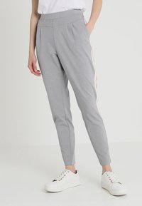 Pantalons gris fuselés en tissu texturé, avec des rayures latérales roses. Taille élastique, deux poches latérales, portés avec des baskets blanches.