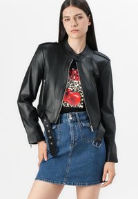 Svart faux skinnjakke med ståkrage, frontglidelås og dekorative knapper. Kombinert med et denim mini-skjørt.
