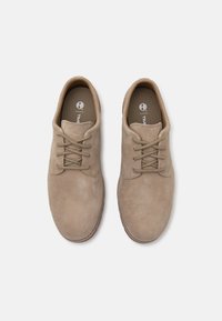 Pantofi din suede bej cu vârf rotunjit, suprafață texturată și șireturi asortate. Brantul de nuanță arămie are un logo; design minimal.