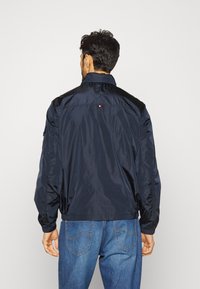 Giacca a vento blu navy con colletto alto, polsini elasticizzati e un piccolo logo sul retro. Tessuto leggero e liscio.