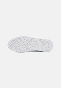 Semelle de chaussure en caoutchouc blanc avec motifs géométriques de la bande de roulement et logo Lacoste embossé près du centre.