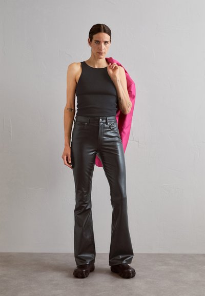 Black ribbed tank top and glossy black flared leather pants. A pink jacket is draped over one shoulder. Chunky black footwear is worn.