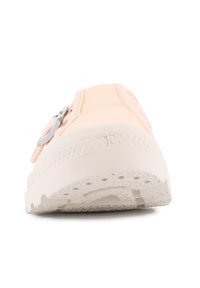 Vista frontale di una sneaker rosa pallido con suola bianca spessa e un accento in fibbia argentata sul lato.