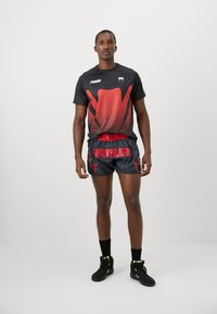 Schwarzes Sportshirt mit rot verlaufendem Design und Punktmuster, kombiniert mit schwarzen Shorts, die roten "VENUM"-Text und Blitzakzente aufweisen.