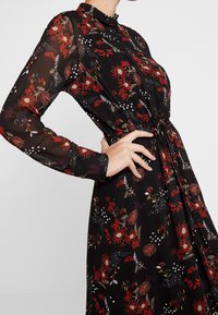 Schwarzes Kleid mit langen Ärmeln, Blumenmuster in Rot, Weiß und Gold, Knopfleiste vorne, tailliert, leichtes durchscheinendes Material.