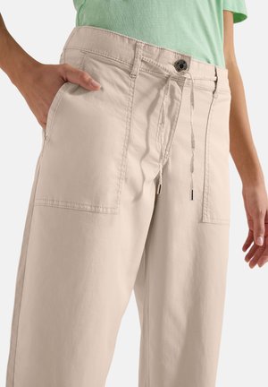 Pantalon beige à jambes larges avec grandes poches plaquées à l’avant, fermeture par bouton et lien coulissant, porté avec un haut vert clair.