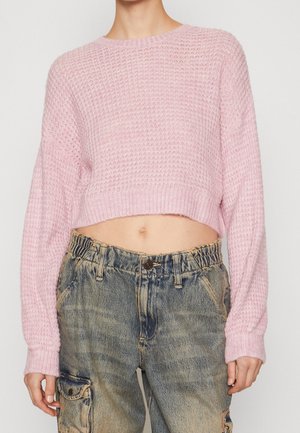 Vrouw draagt een kort, gestructureerd roze trui en hooggetailleerde, losse, uitgebleekte denim cargobroek met zakken.