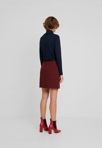 Top a manica lunga blu navy abbinato a una gonna rossa con motivo. Stivali alla caviglia rossi con pannelli neri. Texture liscia, design aderente e lunghezza sopra il ginocchio.
