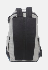 Zaino grigio e nero con pannello posteriore in rete, due tasche laterali, spallacci imbottiti e un comparto superiore con cerniera. Materiale resistente con accenti testurizzati.