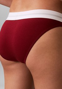 Geribbelde bordeauxrode stoffen ondergoed met een witte tailleband met twee dunne strepen, met een naadloos ontwerp en een aansluitende pasvorm.