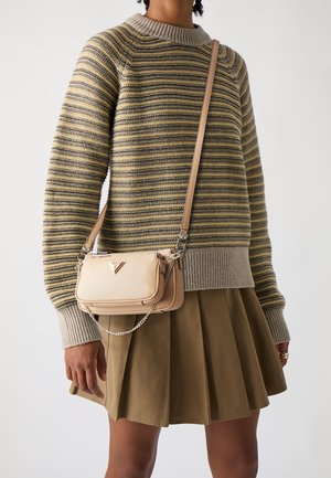 Personne portant un pull en maille rayé, une jupe plissée vert olive, et portant un petit sac bandoulière beige Prada avec détail en chaîne.