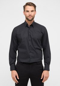 Schwarzes Hemd mit kleinen weißen Punkten, langärmlig und mit Kragen. Glattes Material mit tailliertem Schnitt.