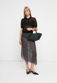 Čierny priesvitný polo top, sukňa polka dot v čierno-bielej farbe s polopriesvitným materiálom a čierna štruktúrovaná kabelka. Vystúpené čierne lodičky dopĺňajú outfit.