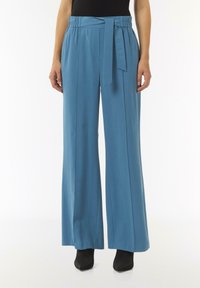 Szerokie spodnie w miękkim, jasnoniebieskim materiale z paskiem w talii. Posiadają gładką teksturę oraz elastyczny pas dla większej wygody.