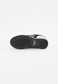 Vista inferiore di una sneaker nera con suola in gomma testurizzata, strisce bianche e dettagli del logo. Presenta una punta arrotondata e un modello di tread robusto.