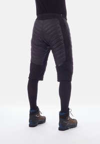 Pantaloni corti neri fino al ginocchio con pannelli imbottiti e una texture liscia. Abbinati a maniche per le gambe scure e traspiranti e scarponi da trekking robusti.