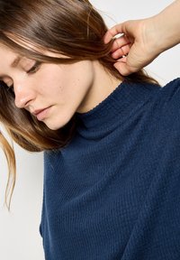 Donkerblauwe gebreide coltrui met een geribbelde structuur. Close-up weergave die de halslijn en stofdetails benadrukt.