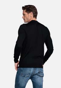 Zwarte lange mouwen trui met een slim fit ontwerp, geribbelde manchetten en zoom, gedragen met een blauwe spijkerbroek, gezien vanaf de achterkant.
