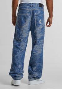 Denim jeans in blue with a faded, distressed pattern. Features a loose fit, multiple pockets, and a logo patch on the back waistband.