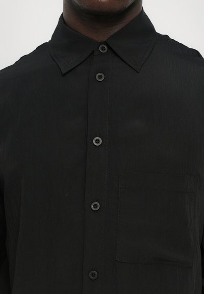 Must teile triiksärk, millel on terav krae, tekstureeritud kangas, eesmine tasku ja mustad nupud. Lihtne disain kaasaegse lõikega.