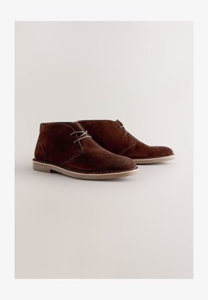 Brune ruskindsankelstøvler med rundet tå, grå snørebånd og lysfarvet gummisål. Simpelt design med syningsdetaljer.