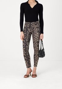 Top negro de manga larga con ribetes, pantalones pitillo con estampado de leopardo en beige y negro, tacones tipo sandalias marrones con tachuelas y un bolso pequeño negro.