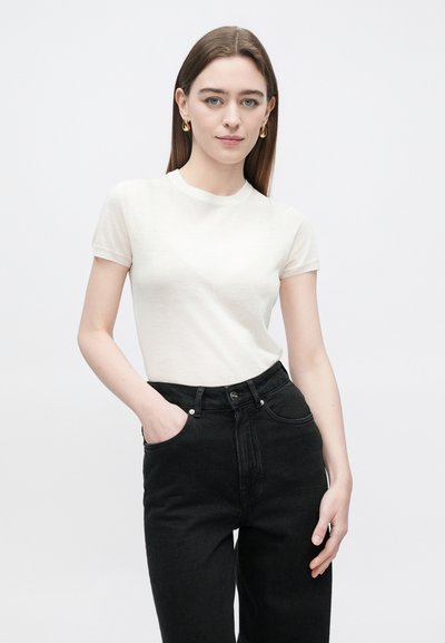 Jasnobeżowa koszulka z krótkim rękawem o okrągłym dekolcie, w połączeniu z czarnymi, wysokim stanem jeansami. Gładka tekstura, dopasowany krój i jednolity kolor.