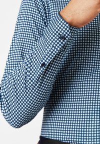 Blau gemusterte Hemd mit einem kleinen Blumendesign, Knopfmanschetten und einer weichen Textur, präsentiert an einem teilweise sichtbaren Arm.