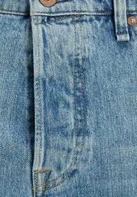 Light blue denim fabric features a diagonal weave, with orange stitching along seams and a brass button at the waistband.