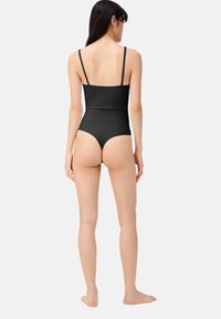 Costume da bagno intero nero con spalline sottili regolabili, un taglio alto sulla gamba e una texture liscia, visto da dietro.