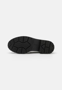 Black rubber shoe sole with a rugged tread pattern, featuring grooves and segmented sections for traction. Brand logo is visible.