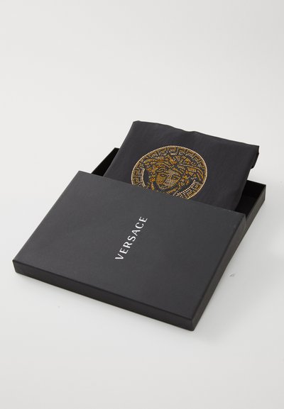Svart låda med en guldaccentuerad Versace-skjorta med cirkulärt mönster. Mjuk textur, prydligt vikta inuti lådan.