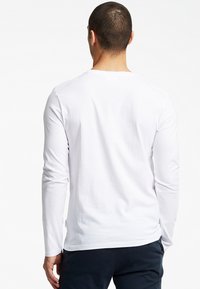 Hvid langærmet skjorte lavet af blødt stof. Har en rund halsudskæring, slim fit og glat tekstur; bæres med mørke bukser.