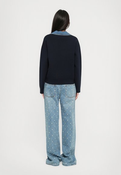 Maglione lavorato a maglia blu navy con colletto in denim, abbinato a jeans azzurri luminosi decorati con applicazioni dorate e argentate.