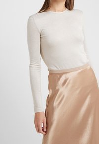 Vaaleanbeige pitkähiha, jossa on hieno kiilto, yhdistettynä sileään, satiinimaiseen vaaleanruskeaan hameeseen, jossa on yksinkertainen vyötärönauha.