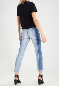 Džínové kalhoty s barevně blokovaným designem, který obsahuje světlé a tmavě modré části, roztrhaný lem, slim fit a nošeny s černými sandály na podpatku.