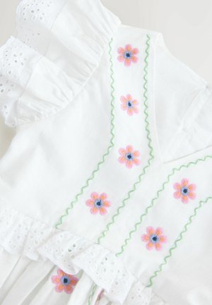 Weißes Baumwollkleid mit gewelltem Spitzenbesatz, grüner Zickzackstickerei und floralen Motiven in Pink und Blau.